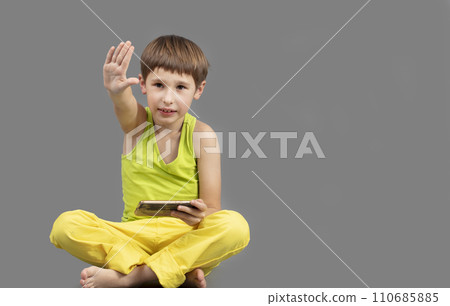 Child on a gray background with a mobile phone with a raised hand. Child on a gray background with a mobile phone with a raised hand. 110685885