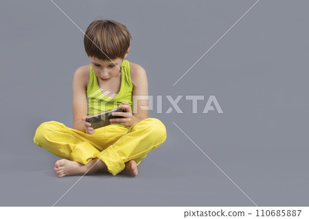 Child on a gray background with a mobile phone. The boy plays in the smartphone. Child on a gray background with a mobile phone. The boy plays in the smartphone. 110685887