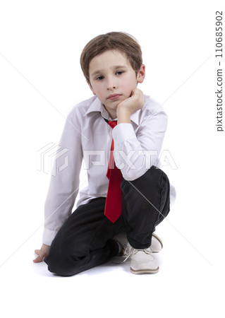The child sits on a white background. Dressy boy in a white shirt isolated. Seven year old child in a tie. Primary school student. The child sits on a white background. Dressy boy in a white shirt isolated. Seven year old child in a tie. Primary school student. 110685902