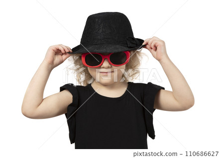 Funny little girl in a black hat and sunglasses on a white background. Beautiful fashionable child. Funny little girl in a black hat and sunglasses on a white background. Beautiful fashionable child. 110686627