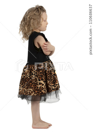 A little girl is standing right in profile. The little curly-haired baby girl is barefoot. Funny child.Full length portrait of a cute little girl. A little girl is standing right in profile. The little curly-haired baby girl is barefoot. Funny child.Full length portrait of a cute little girl. 110686637