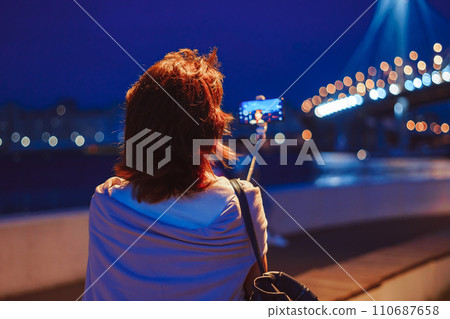A girl takes pictures of herself on her phone at night in the city 110687658