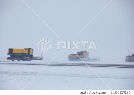 Snow plows removing snow from runway during snowfall. 110687925