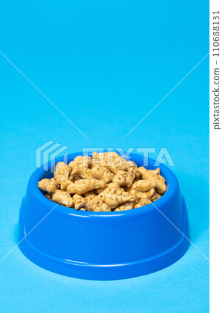 A treat for cats and kittens is a fish-shaped catnip cookie in a blue bowl, copy space for text. A treat for cats and kittens is a fish-shaped catnip cookie in a blue bowl, copy space for text. 110688131