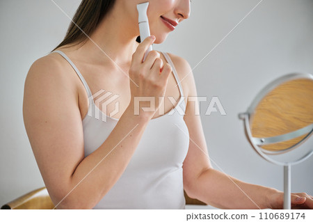 A woman in her 30s shaving her face with an electric shaver A woman in her 30s shaving her face with an electric shaver 110689174