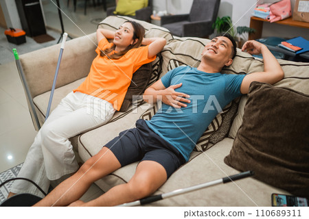 asian couple laying down on sofa after cleaning house asian couple laying down on sofa after cleaning house 110689311