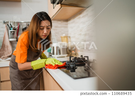 asian female focused on wiping stove asian female focused on wiping stove 110689435