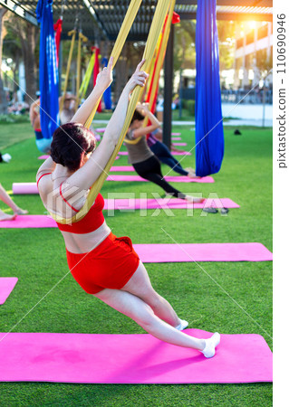 Stretching the body muscles on air suspended fabrics. Group lesson outdoors Stretching the body muscles on air suspended fabrics. Group lesson outdoors 110690946
