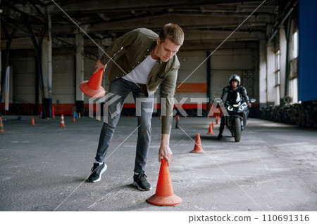 Motorbike driving school lesson with instructor putting cone on track Motorbike driving school lesson with instructor putting cone on track 110691316