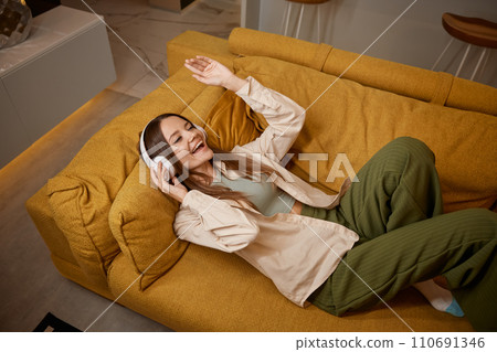 Happy relaxed young woman listening music in headphones at home Happy relaxed young woman listening music in headphones at home 110691346