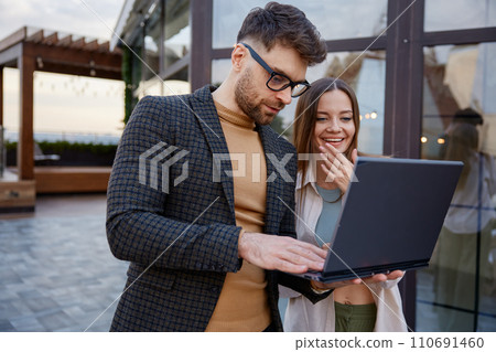 Man and woman using laptop standing together on roof terrace 110691460