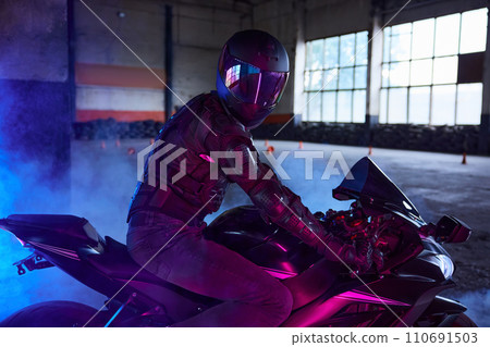 Portrait of motor biker wearing protective gear and helmet in neon light 110691503