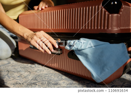 Closeup woman closing zipper of suitcase after packing stuff for journey trip Closeup woman closing zipper of suitcase after packing stuff for journey trip 110691634