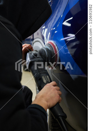 Man with an orbital polisher in car workshop polishing car closeup Man with an orbital polisher in car workshop polishing car closeup 110691982
