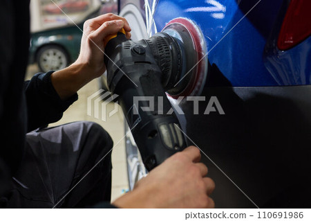 Man with an orbital polisher in car workshop polishing car closeup 110691986