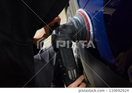 Man with an orbital polisher in car workshop polishing car closeup 110692024