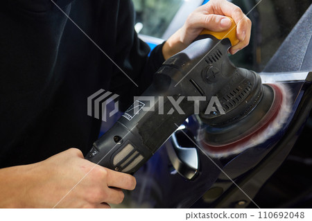 Man with an orbital polisher in car workshop polishing car closeup Man with an orbital polisher in car workshop polishing car closeup 110692048