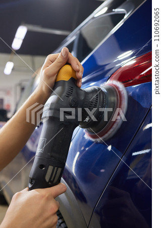 Man with an orbital polisher in car workshop polishing car closeup 110692065