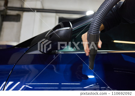 Man worker drying car on wash. Service car wash express. Worker uses turbo dryer to remove drops of water. Detailing, car wash, and paint correction concept. Close-up 110692092