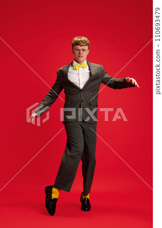 Full-length portrait of young man in formal wear with yellow bright socks dancing against red studio background 110693479