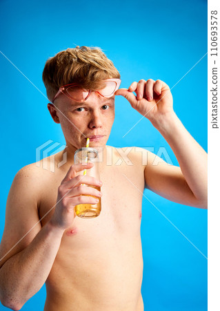 Portrait of young redhead man in stylish pink sunglasses sipping lemonade against blue studio background. Portrait of young redhead man in stylish pink sunglasses sipping lemonade against blue studio background. 110693578