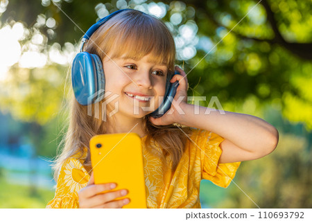 Happy child girl in wireless headphones choosing, listening music in smartphone dancing outdoors 110693792
