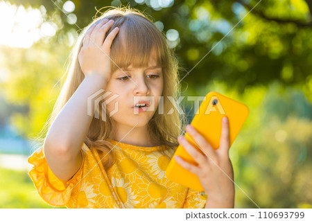 Surprised child girl play game use smartphone loses, bad news, fortune loss fail on city park street 110693799