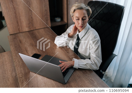 Exhausted middle-aged business woman having neck pain, pinched nerves, tensed sore muscles, cervical osteochondrosis. High-angle view of tired female entrepreneur with pain neckache works at laptop. Exhausted middle-aged business woman having neck pain, pinched nerves, tensed sore muscles, cervical osteochondrosis. High-angle view of tired female entrepreneur with pain neckache works at laptop. 110695094