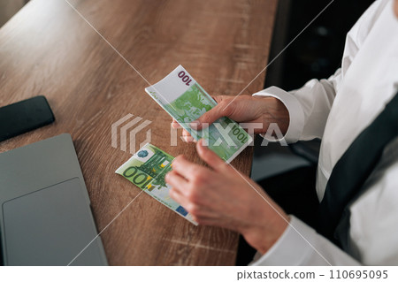 Top view of woman sitting at table, holding euro bills in hands, counting money. Closeup cropped shot of female counting European currency. Concept of financial accounting budget planning 110695095