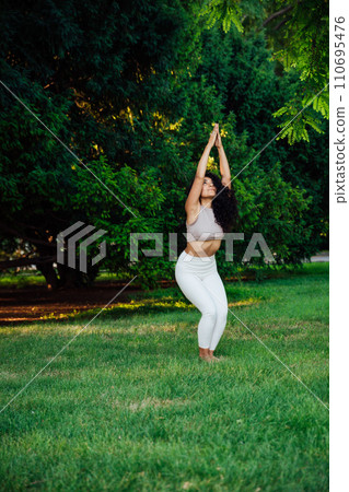 Young brunette asian woman practicing yoga during workout in park Young brunette asian woman practicing yoga during workout in park 110695476