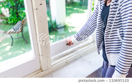 Portrait of a person opening a white frame window from a bright interior 110695520