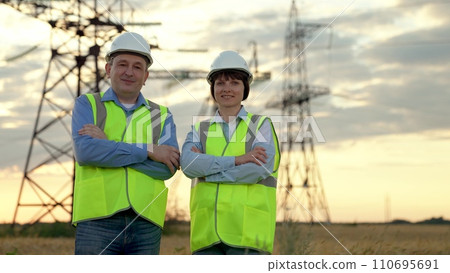 Happy workers stand crossing arms against electric power transmission lines 110695691