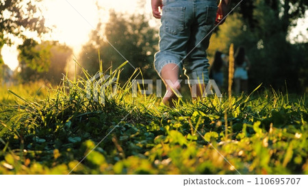 Little contented child joyfully dashes barefoot on grass in park in warm weather Little contented child joyfully dashes barefoot on grass in park in warm weather 110695707
