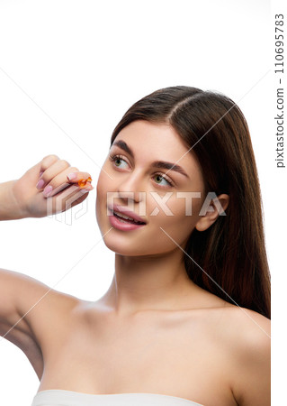 Portrait of naturally beautiful, brunette woman with perfect long, silky and healthy hair showing hair-care oil capsule and looking away. 110695783