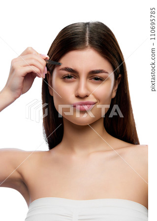 Young emotional girl with tweezing her eyebrows and looking at camera giving attention to beauty and facial grooming against white studio background. 110695785