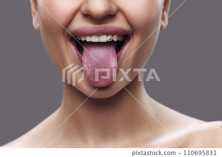 Cropped photo. Close-up of female mouth with tongue, highlighted by subtle lip gloss, against gray background. Cropped photo. Close-up of female mouth with tongue, highlighted by subtle lip gloss, against gray background. 110695831