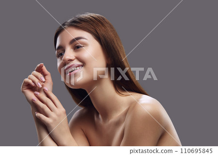 Portrait of young brunette woman with pleasant appearance posing and smiling against grey studio background. Concept of natural beauty people. 110695845