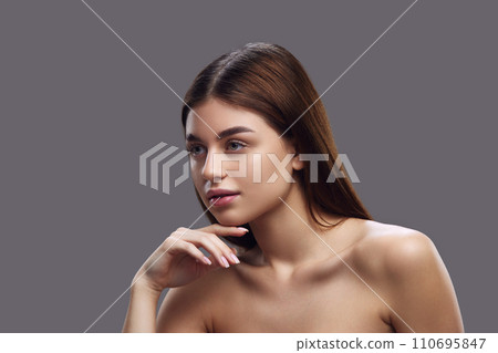 Side profile of brunette woman with sleek hair and bare shoulders, gracefully and elegantly posing against grey background. Side profile of brunette woman with sleek hair and bare shoulders, gracefully and elegantly posing against grey background. 110695847