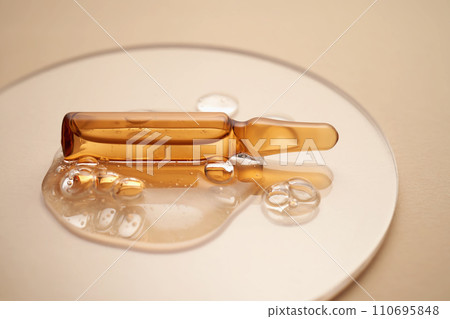 Ampoule in a drop of cosmetic gel on a beige background. Ampoule in a drop of cosmetic gel on a beige background. 110695848