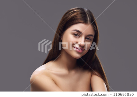 Young brunette woman with perfect, clean and smooth skin looking at camera against grey studio background. Concept of beauty, make up. 110695850