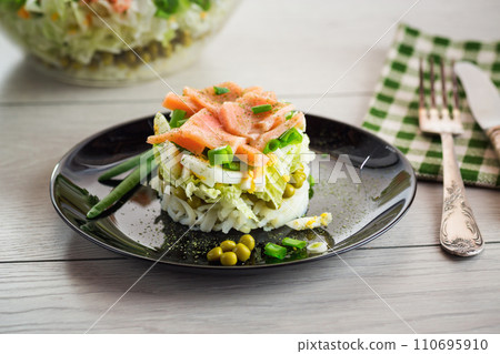 Layered salad of cabbage and other vegetables with pieces of red fish in a plate. 110695910