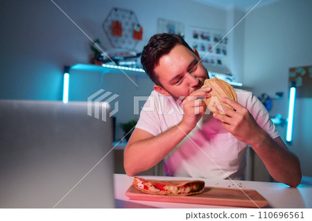 a young man, wearing latex gloves, preparing a falafel sandwich in a pita bread, with chopped tomato and onion 110696561