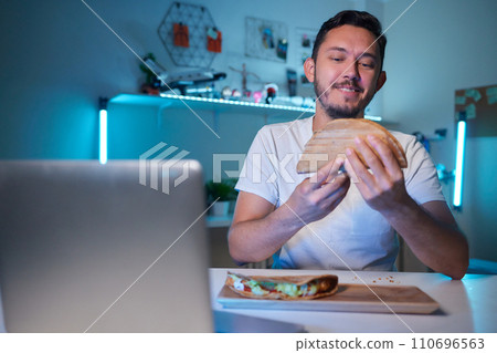 a young man, wearing latex gloves, preparing a falafel sandwich in a pita bread, with chopped tomato and onion a young man, wearing latex gloves, preparing a falafel sandwich in a pita bread, with chopped tomato and onion 110696563