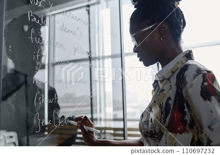 Young african american office employee writing code with white marker on glass board Young african american office employee writing code with white marker on glass board 110697232