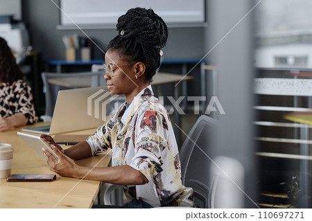 Side view shot of young black girl with dreadlocks working on tablet sitting at office desk 110697271