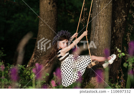 A small and beautiful girl in a dress is swinging on a swing. 110697332