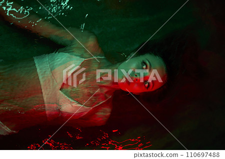 Scared woman floats in red-lit water at night, terrified expression, lagoon swimming, psychological themes of calm, dual self, introspection. Female frightened by unknown thoughts. Scared woman floats in red-lit water at night, terrified expression, lagoon swimming, psychological themes of calm, dual self, introspection. Female frightened by unknown thoughts. 110697488