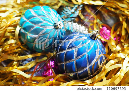 Christmas balls, foil cones and decorations with gold tinsel close-up. Beautiful bright decorative balls of a modern fashionable design with intertwining stripes. New Year's and Christmas Xmas 110697893