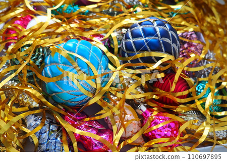 Christmas balls, foil cones and decorations with gold tinsel close-up. Beautiful bright decorative balls of a modern fashionable design with intertwining stripes. New Year's and Christmas Xmas 110697895