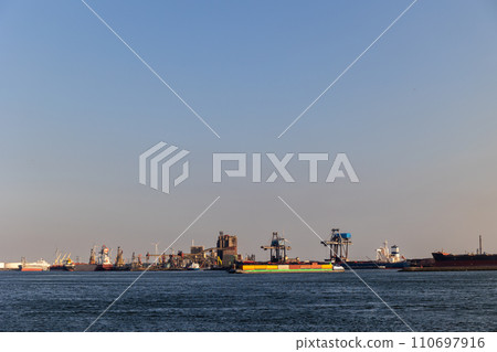 Ships float across the North Sea. Windmills in the background. Slow motion. Sea port in the Netherlands. A lot of cranes for loading goods. Different ships and barges. Ships float across the North Sea. Windmills in the background. Slow motion. Sea port in the Netherlands. A lot of cranes for loading goods. Different ships and barges. 110697916